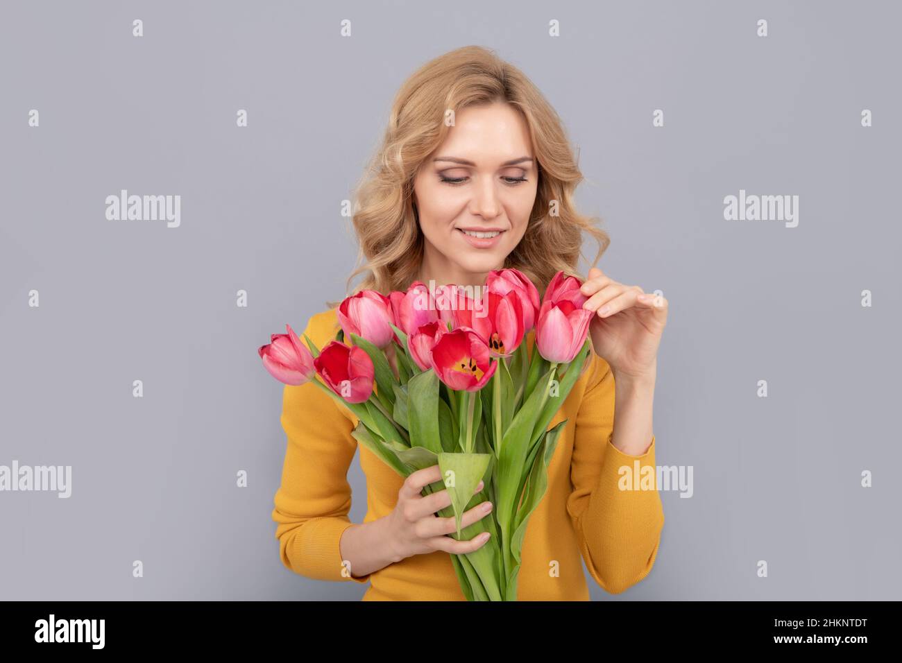 positive lady hold flowers for spring holiday on grey background Stock Photo