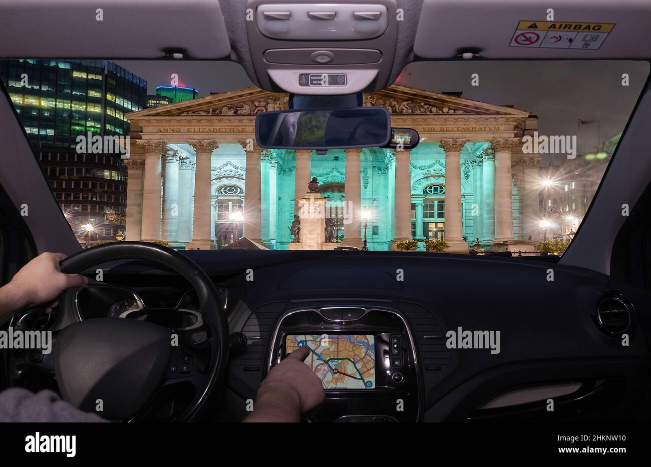 Driving a car while using the touch screen of a GPS navigation system towards the Royal Exchange Building in the financial district of London, UK Stock Photo