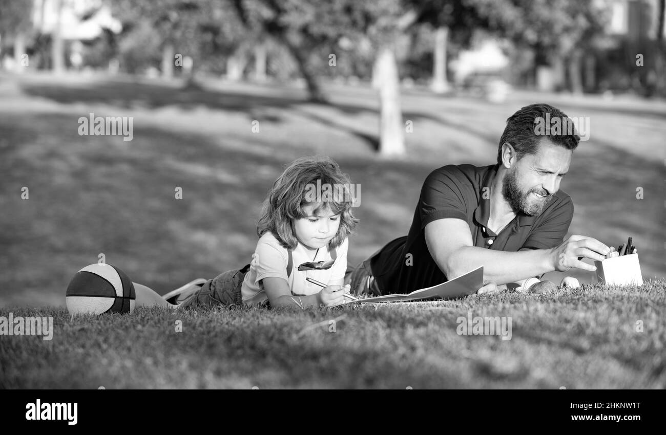 happy family day. dad and kid boy relax on grass in park. child hold learning to draw. Stock Photo