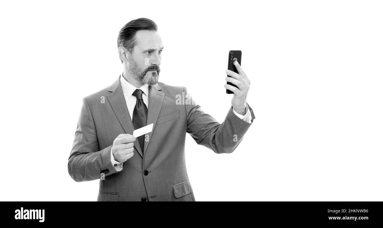 serious mature boss in suit hold credit card and phone isolated on white, selfie Stock Photo