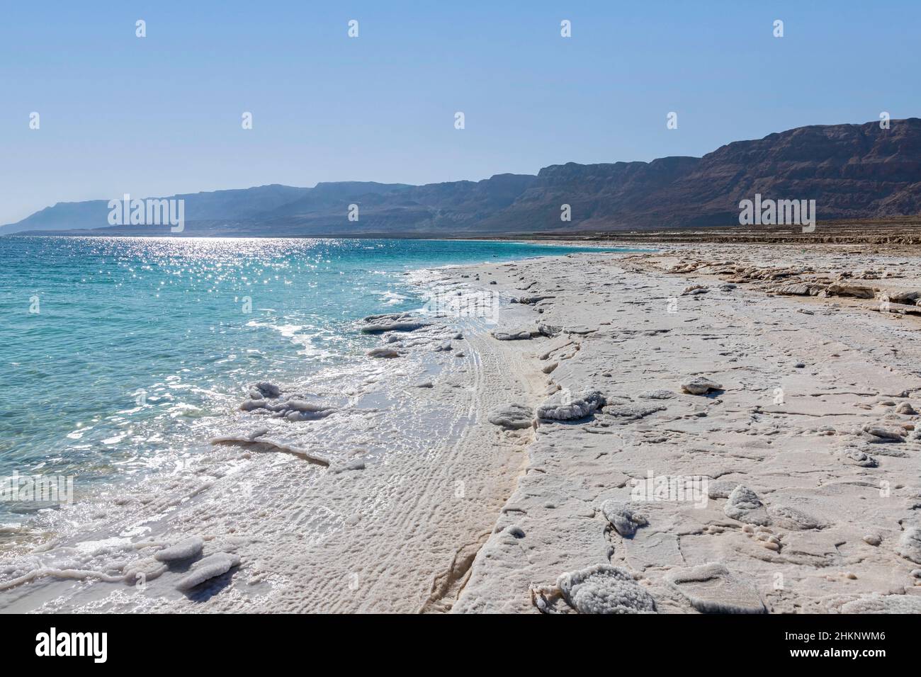 View of the mountains across the waters of the Dead Sea from the shore covered with salt formations. Stock Photo