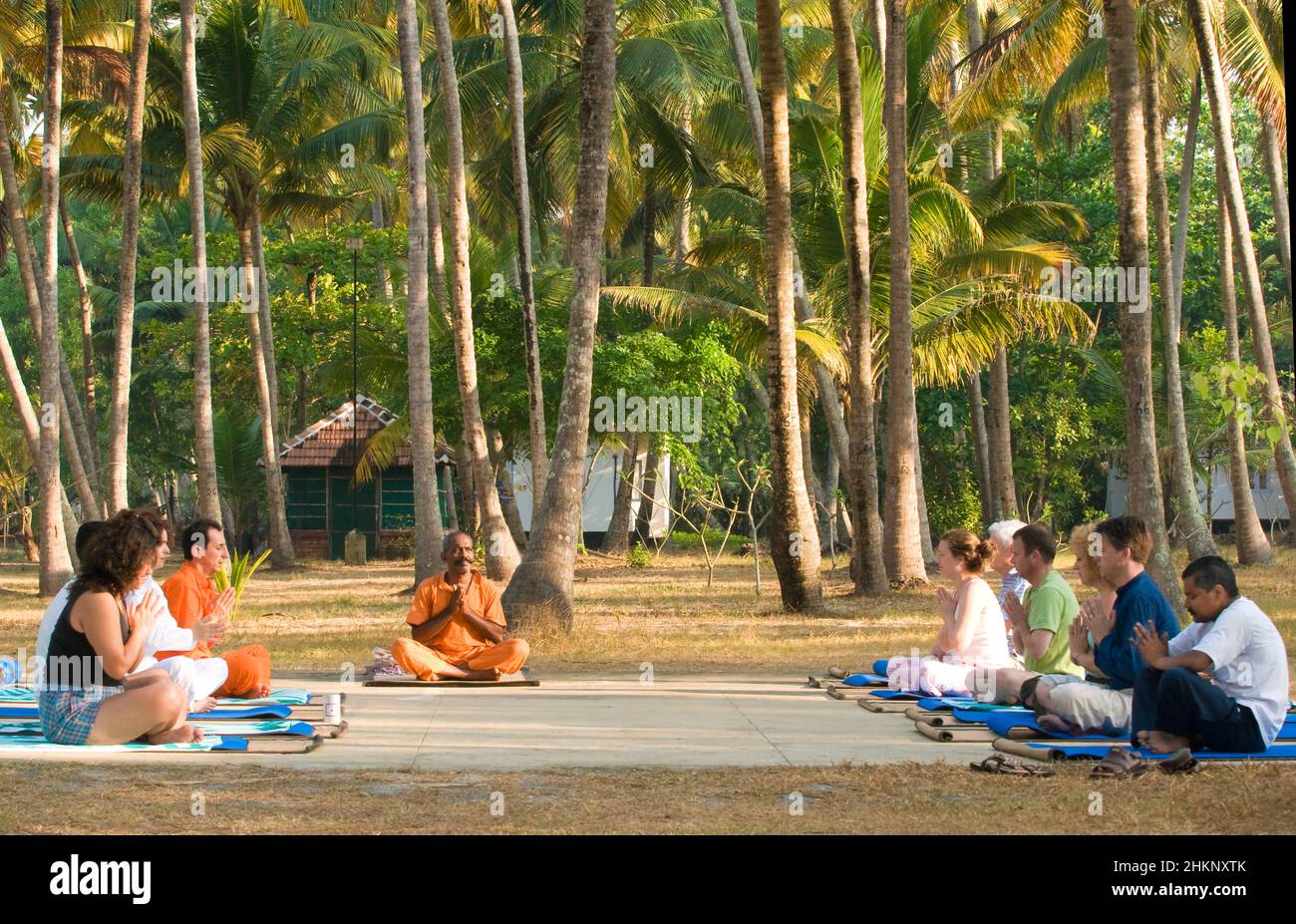 Yoga teacher with pupils seated outdoors surrounded by palm trees in Kerala, India Stock Photo