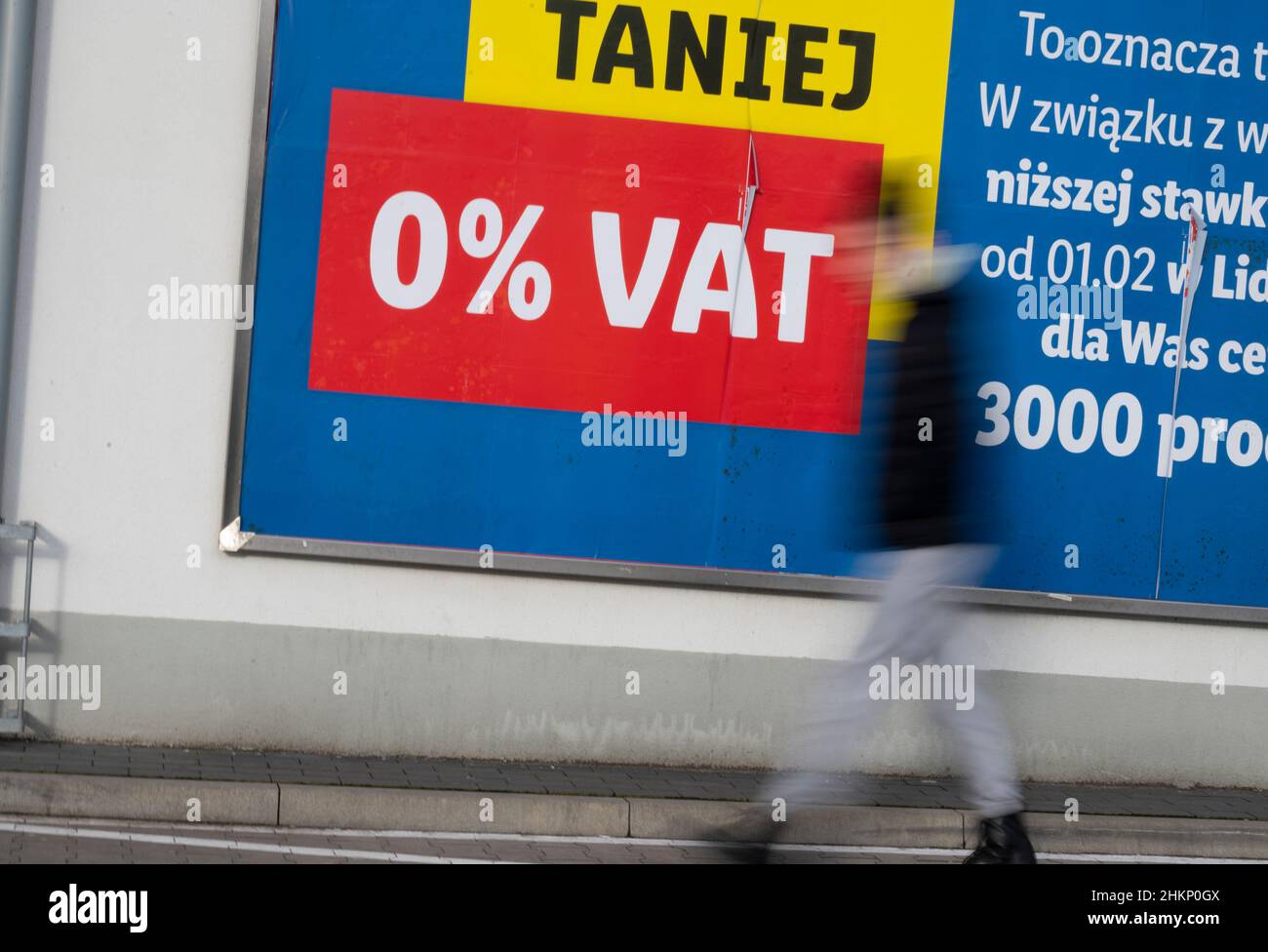 Slubice, Poland. 05th Feb, 2022. A man walks with a shopping cart in front of an advertising poster with the inscription 'Taniej - 0% VAT' (Cheaper - 0% VAT). Due to a reduction in VAT on food and fuel from 23 to 8 percent, food in Poland is sometimes significantly cheaper than in Germany. Credit: Christophe Gateau/dpa/Alamy Live News Stock Photo