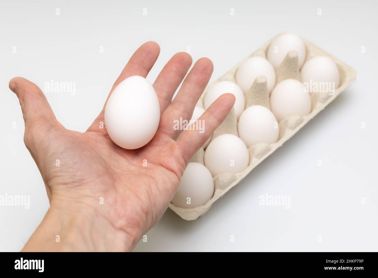 a hand holds an egg in the palm of a hand against a background of a dozen eggs Stock Photo