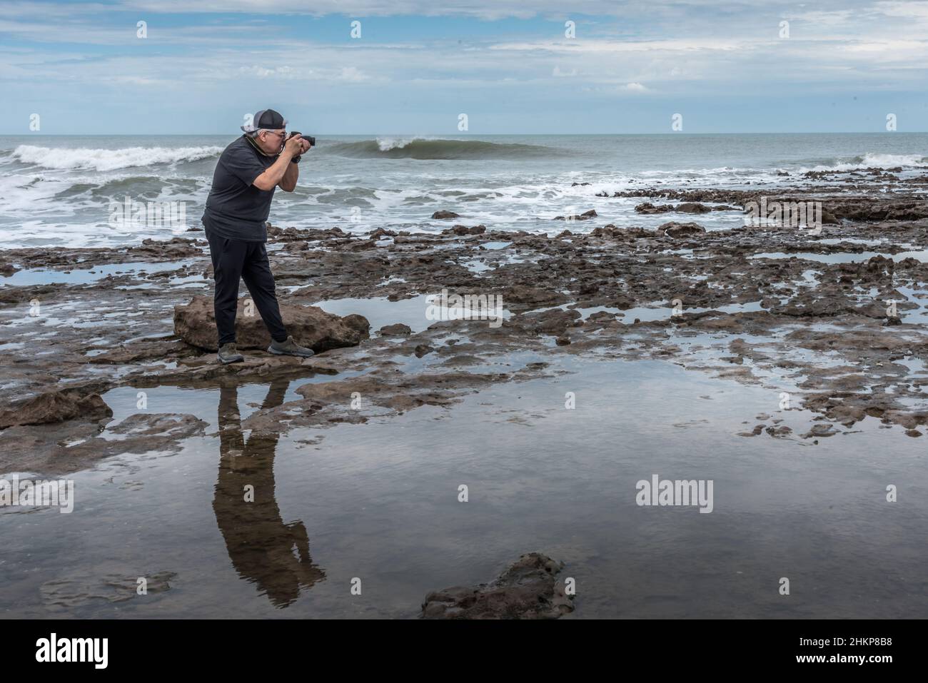 Mature adult man taking a photo on the rocks near the sea. Stock Photo