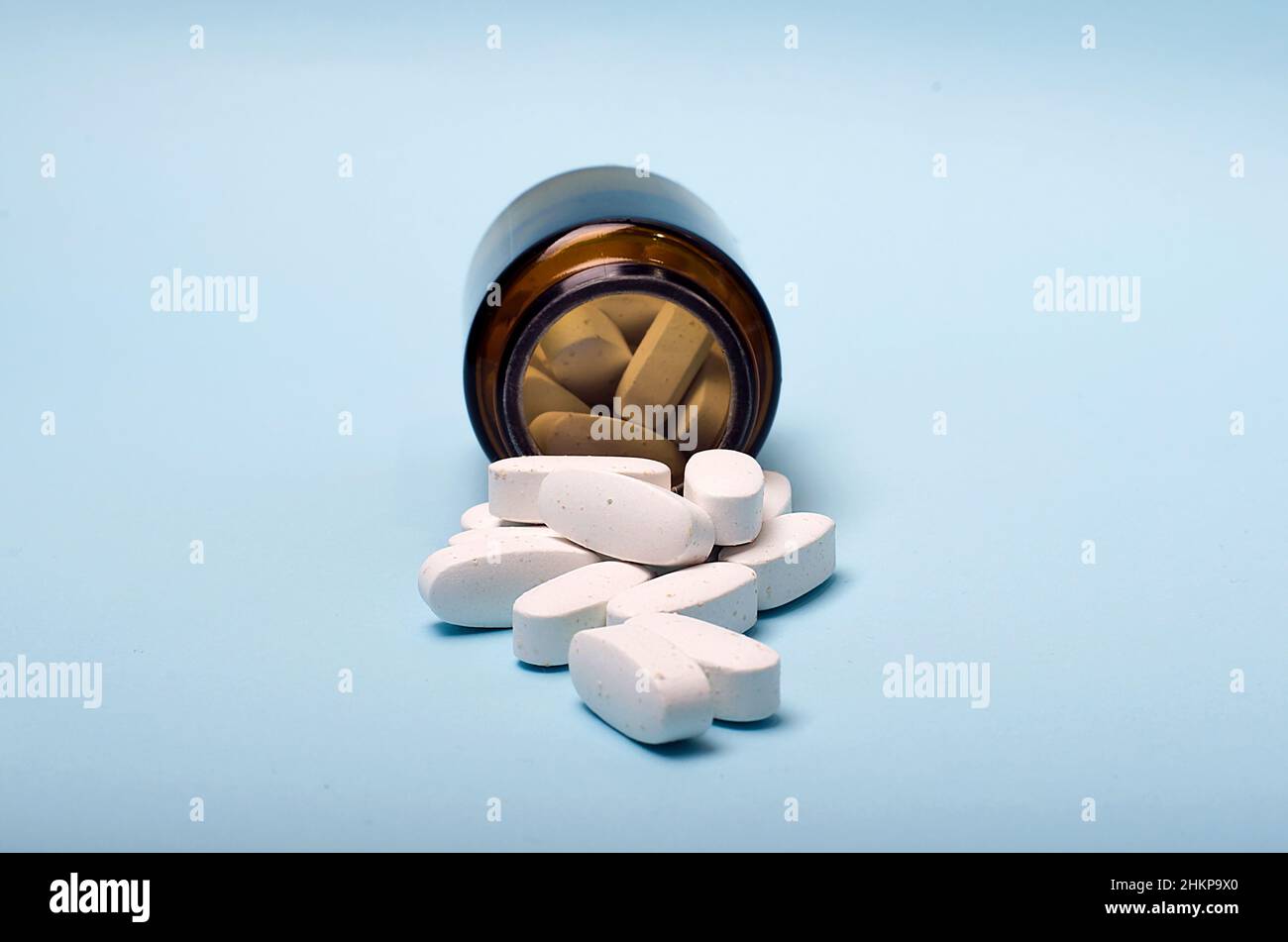 White large pills are pouring out of a glass medical jar on a blue medical background. Center pills.Photo for a medical clinic, pharmacy. Stock Photo