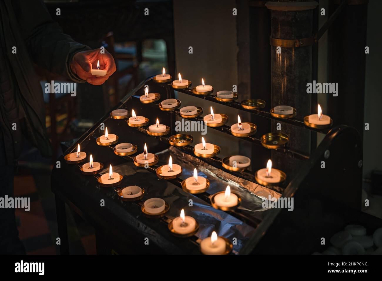 Hand holding a lit candle, putting it on altar. Candles are lit for