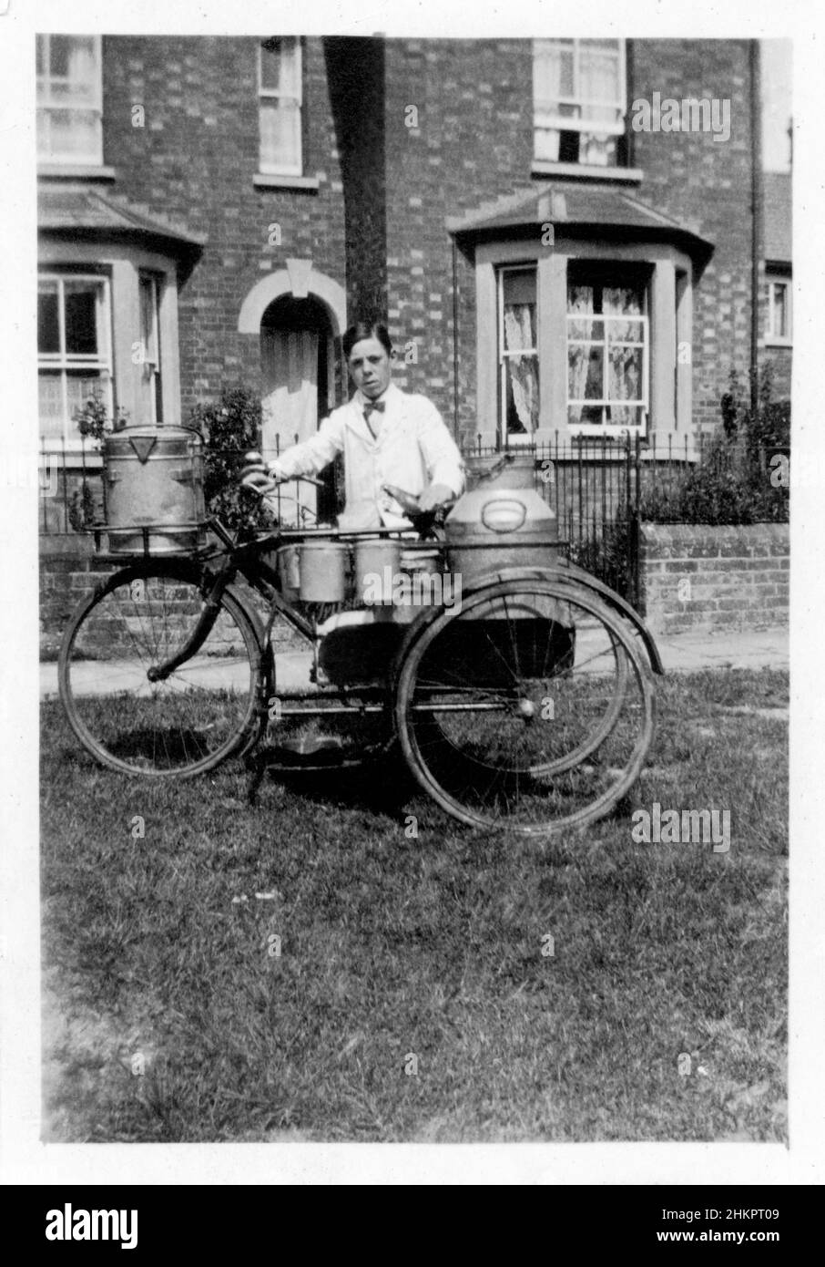 Milk boy  wearing a white coat and bow tie, delivering milk and cream on a tricycle. Stock Photo