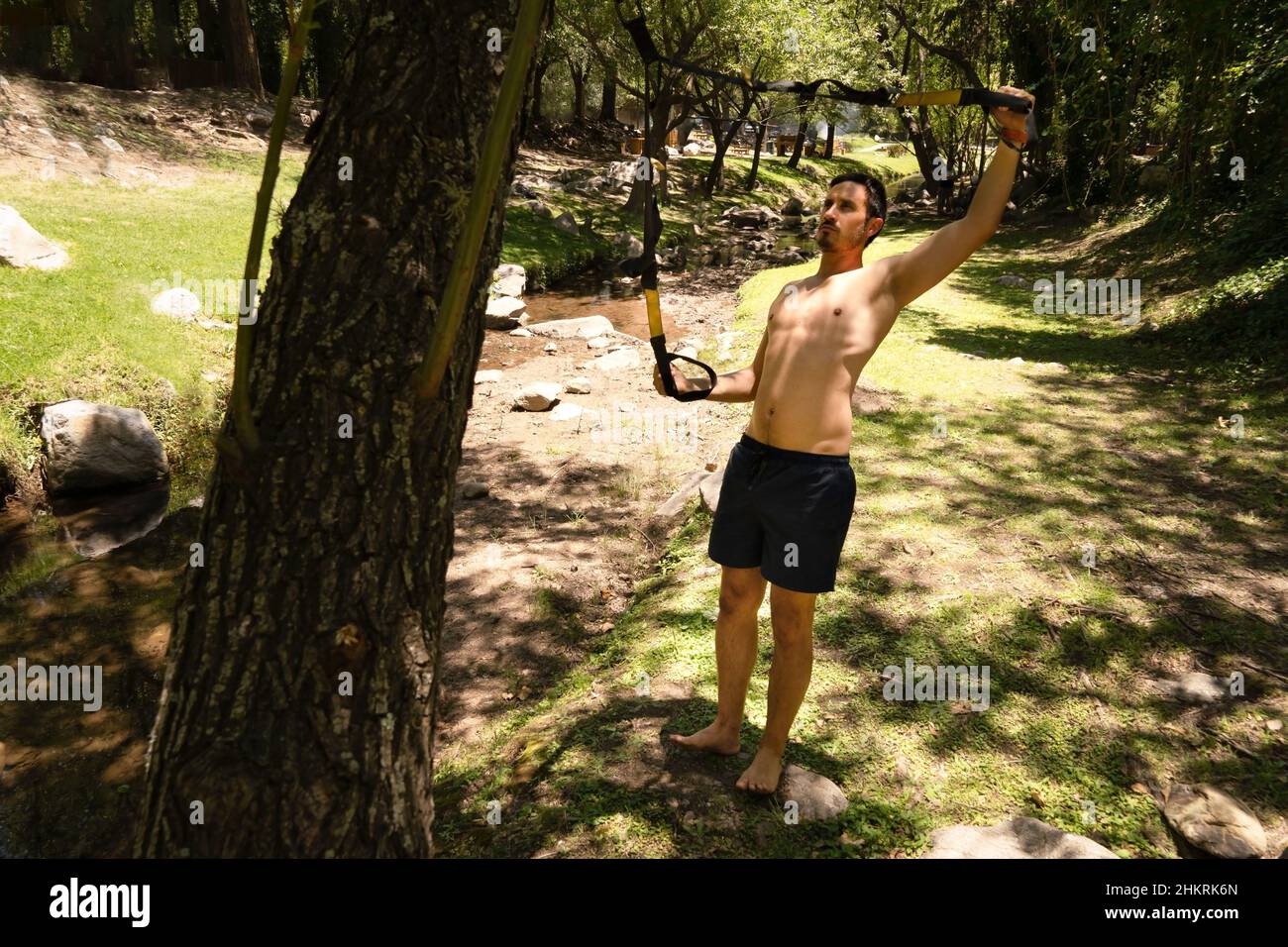 Handsome muscular man is training outdoor on TRX. Total Body Resistance Exercises. Stock Photo