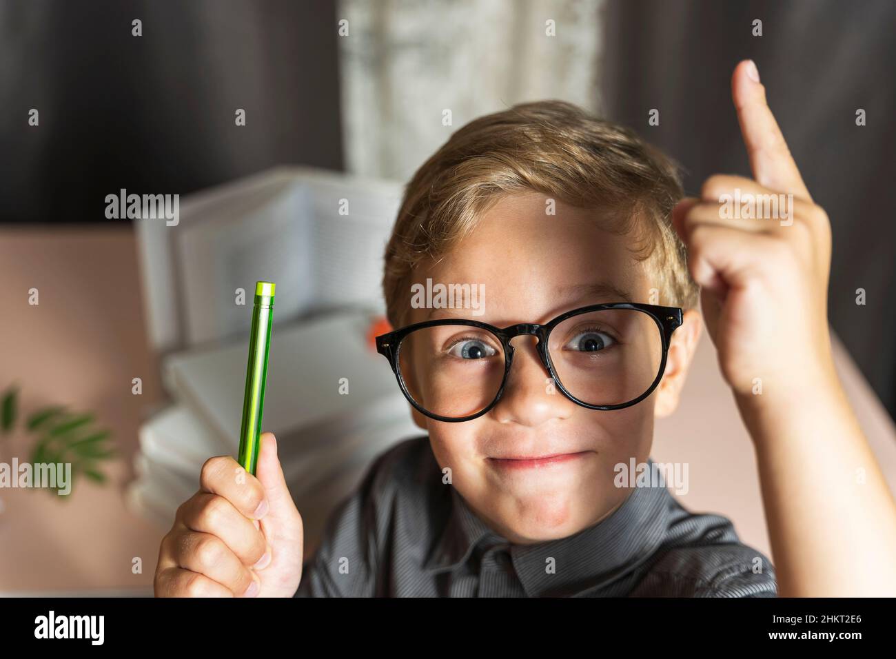 A smart boy with glasses enthusiastically raises his finger up, the concept of learning, curiosity and new discoveries, against the background of text Stock Photo