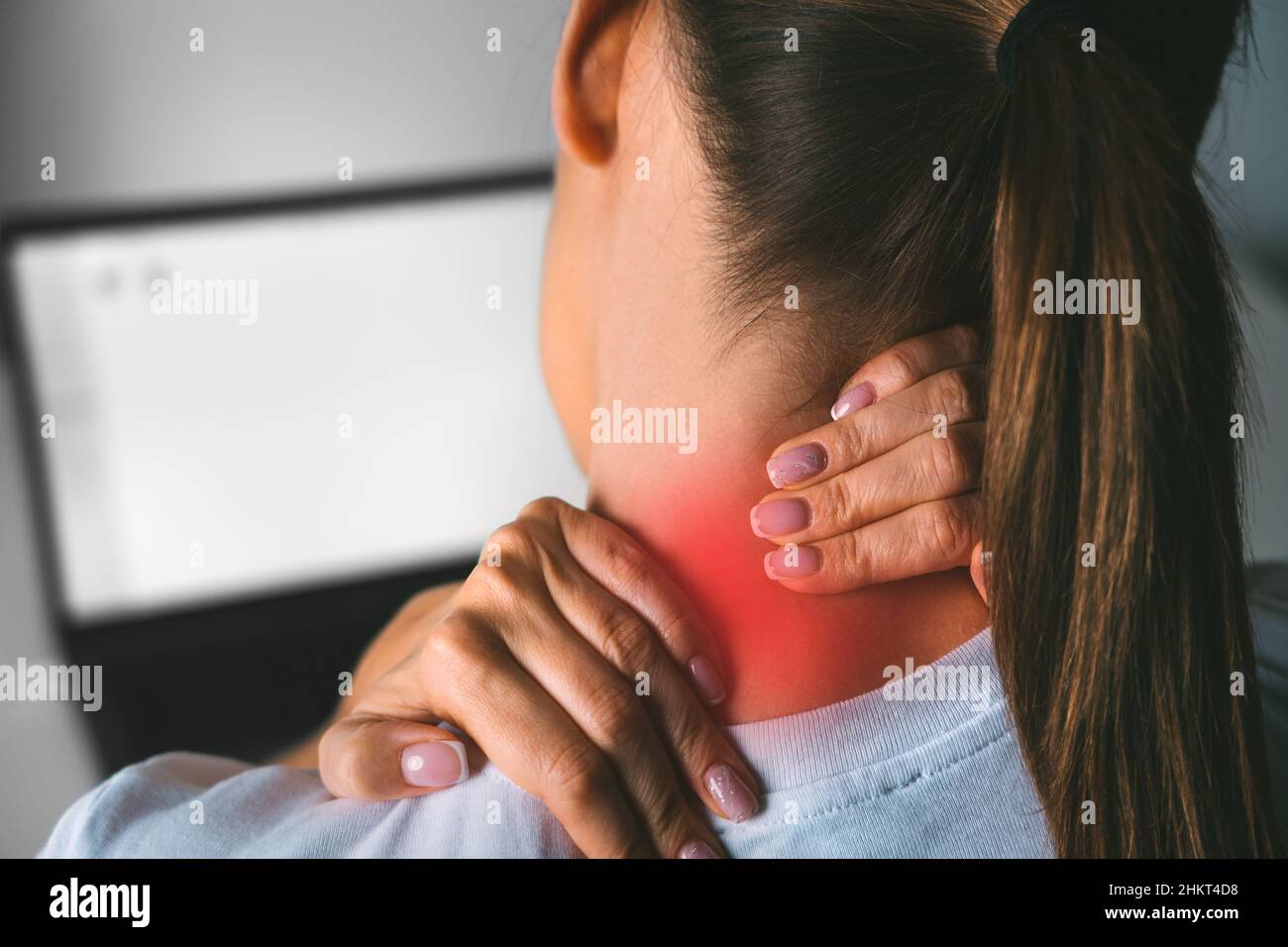 Neck pain after working on computer. Young woman massaging neck to relieve pain after working on pc Stock Photo