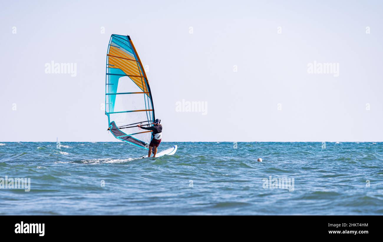 A man controls a sailboard at sea: one of the best remedies for a pandemic is windsurfing, and no mask is needed! Stock Photo