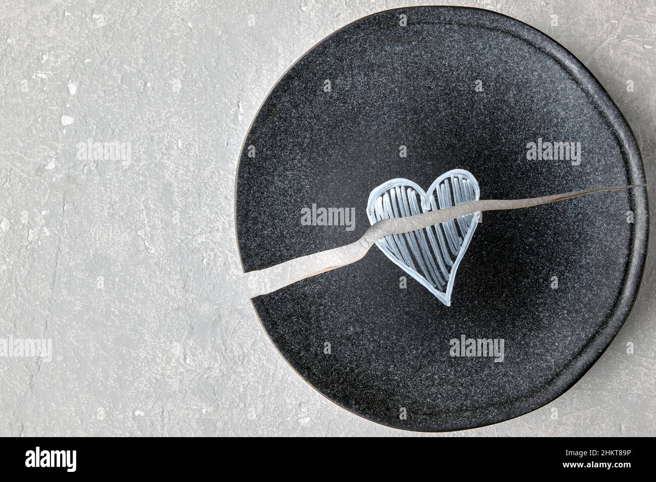 A broken ceramic plate with a painted heart on a light concrete table Stock Photo