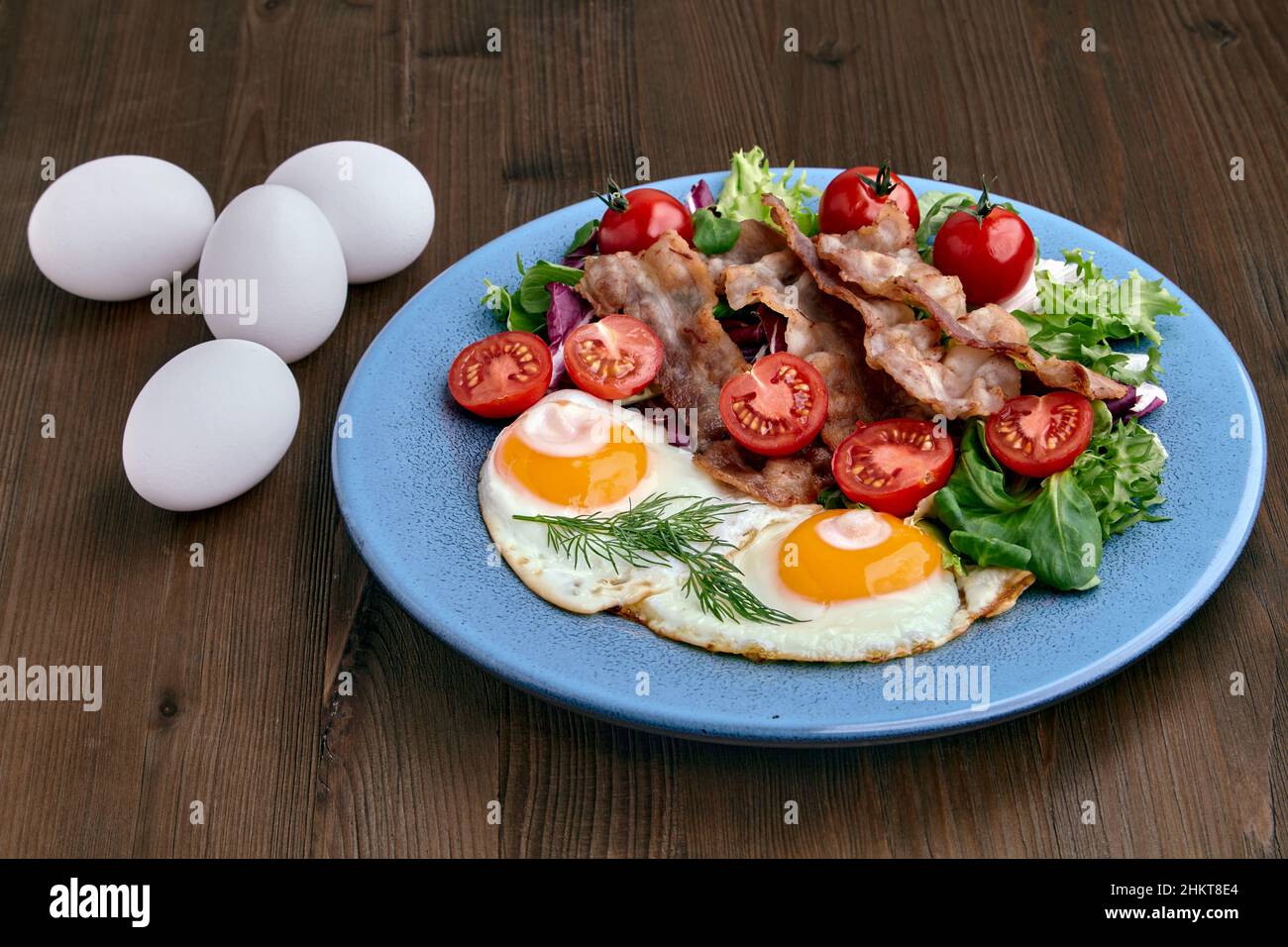 Fried eggs with bacon, lettuce and cherry tomatoes on a blue plate Stock Photo