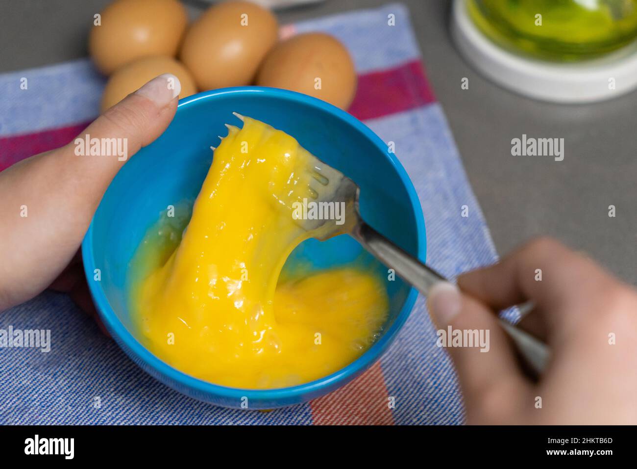 beating hen's eggs in a blue bowl with a fork Stock Photo