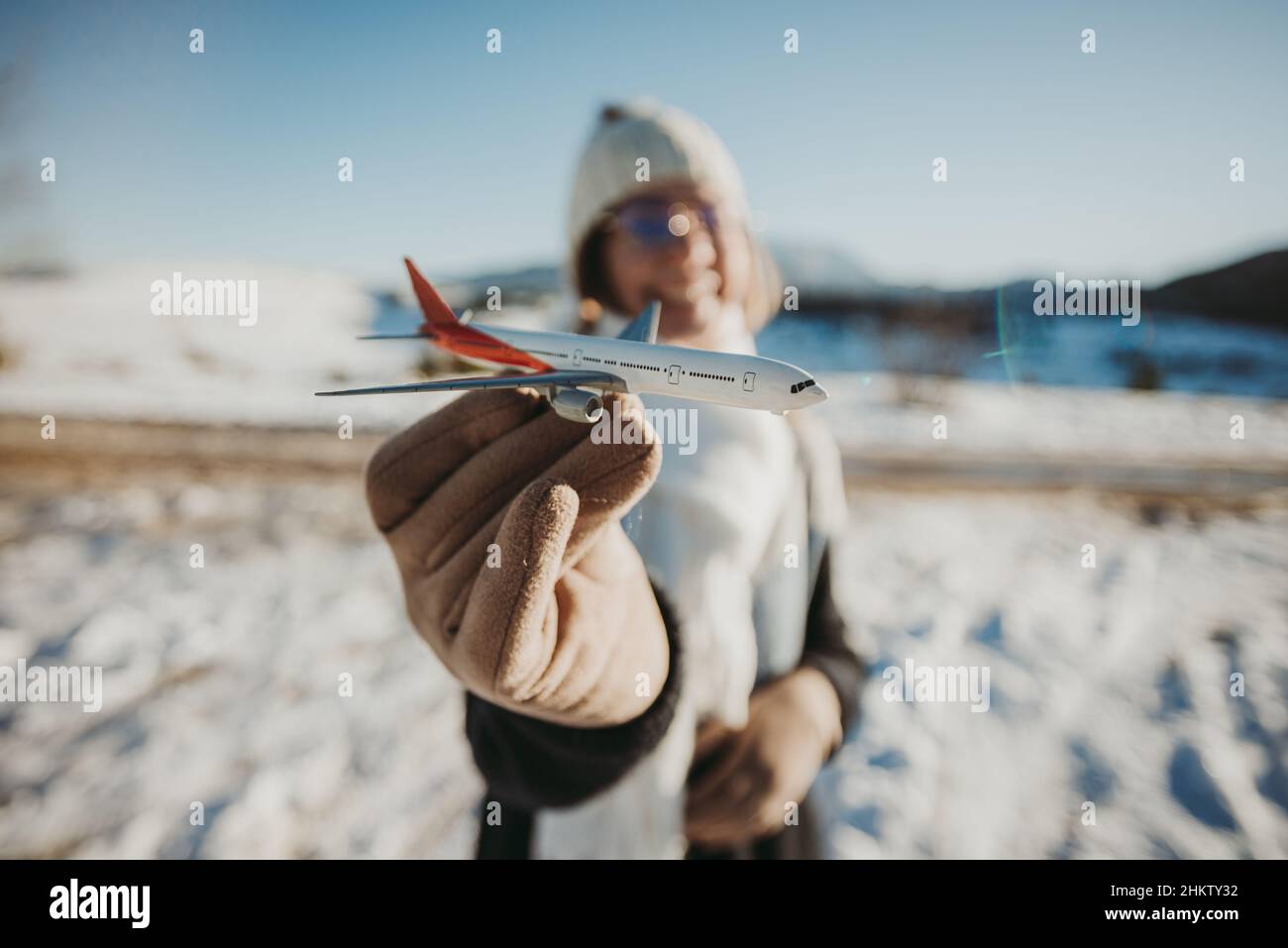 Selective focus shot of a toy airplane on smiling Caucasian female's hand while in snowy outdoors Stock Photo