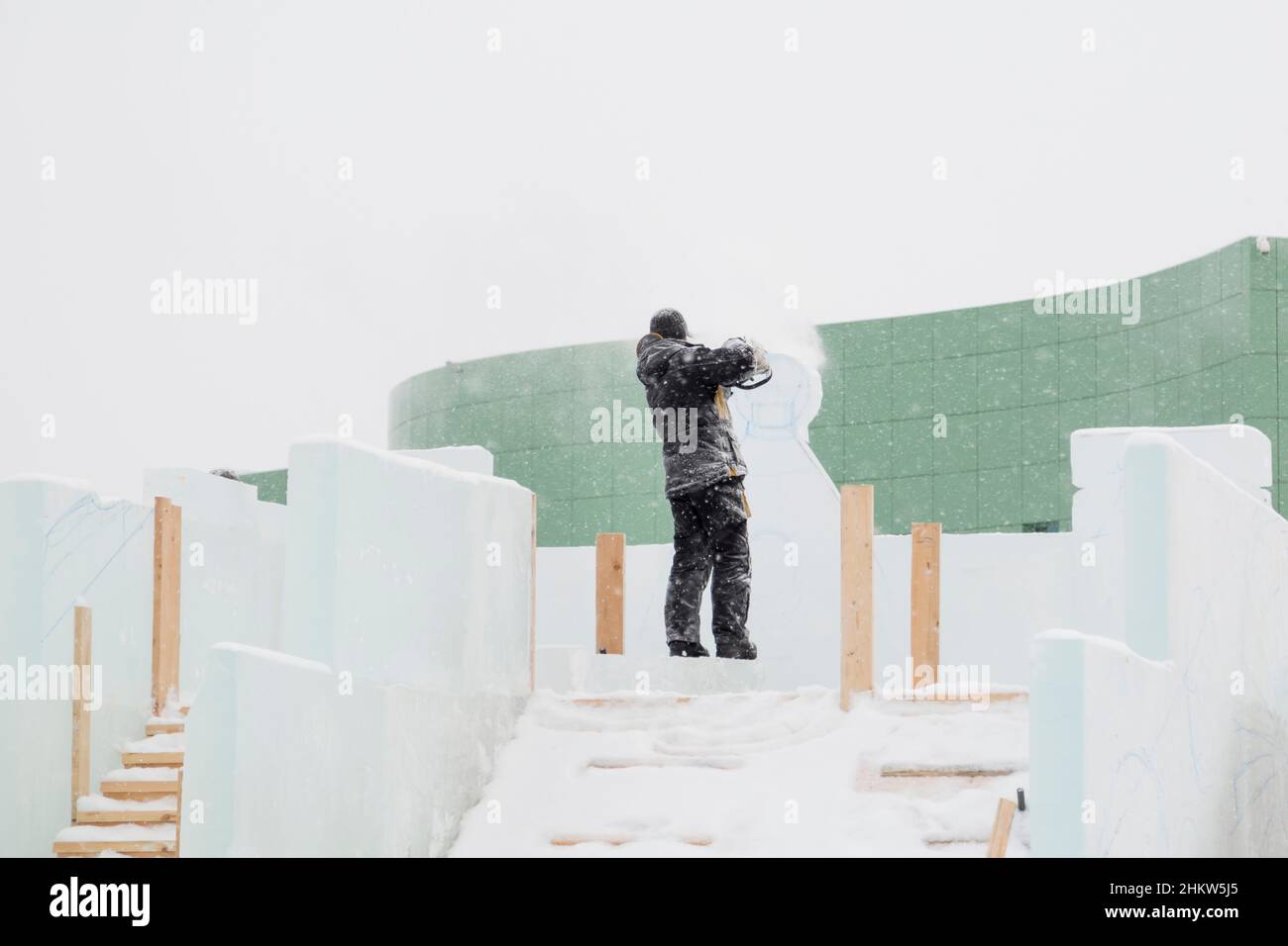 The sculptor cuts out the contours of the future composition with a chainsaw in an ice slab Stock Photo