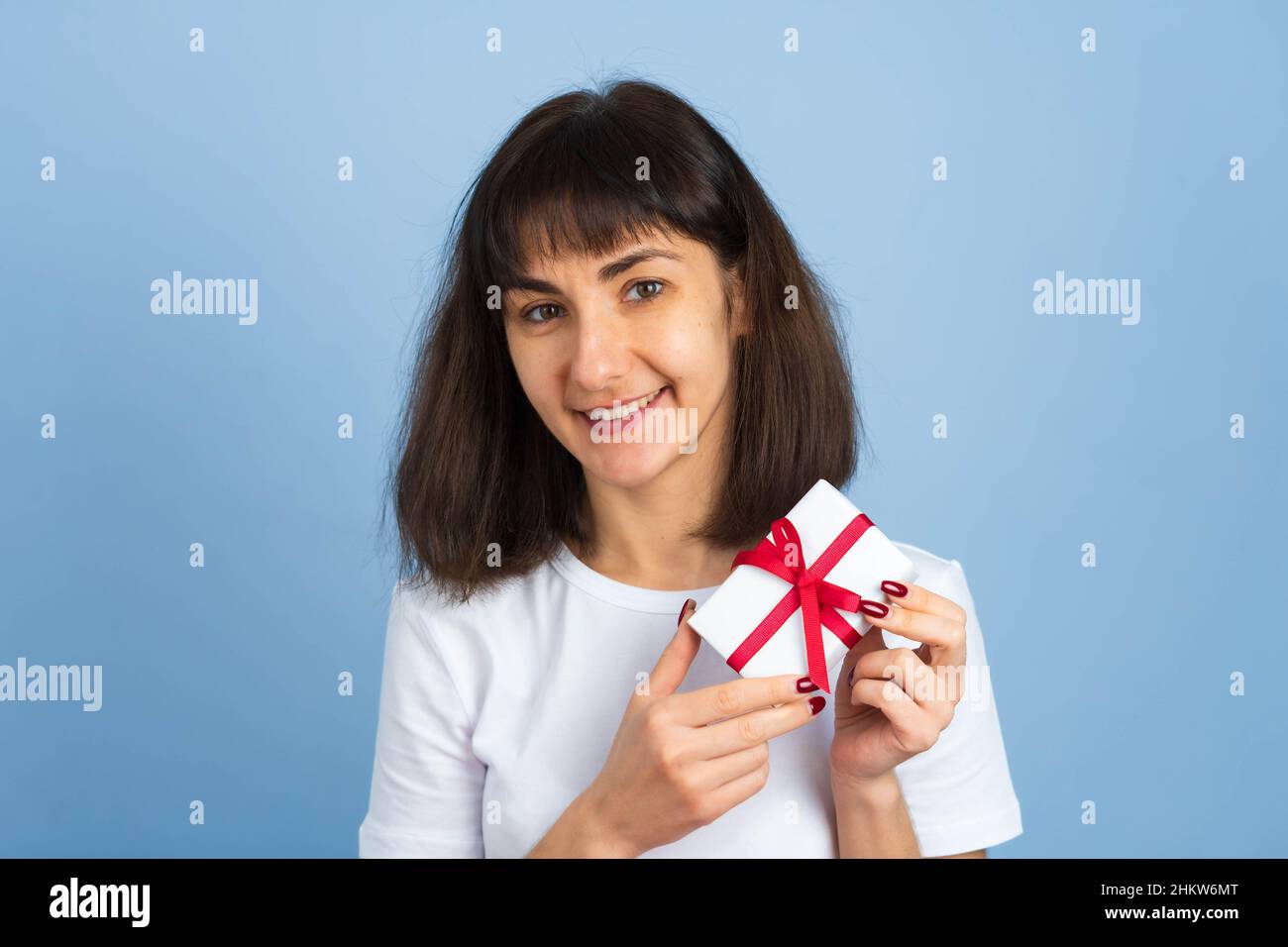 Smiling happy woman holding gift box isolated on blue background. Valentines day or birthday concept Stock Photo