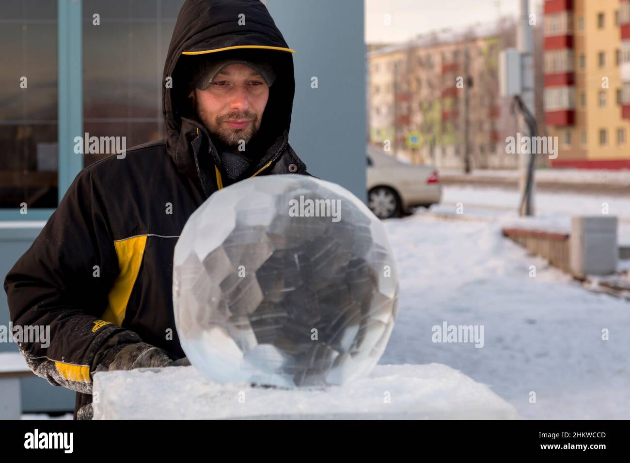 A sculptor carves a round ice ball out of a block of ice with a chisel ...