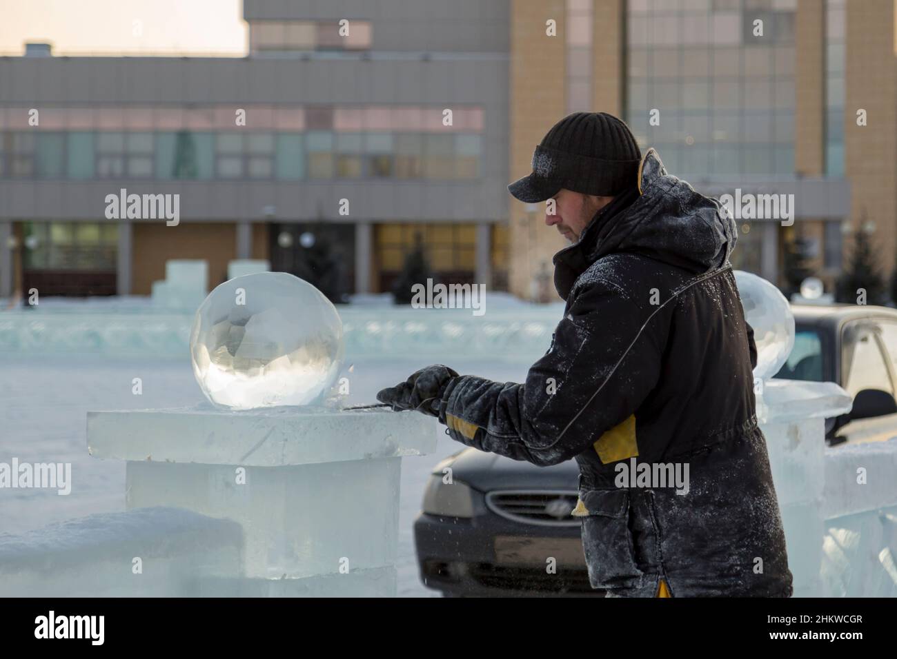 A sculptor carves a round ice ball out of a block of ice with a chisel ...