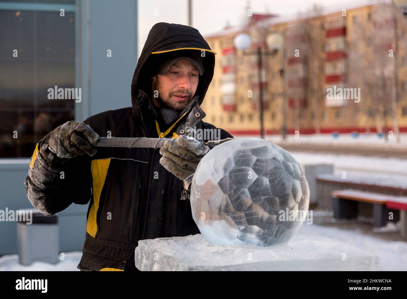 A sculptor carves a round ice ball out of a block of ice with a chisel ...