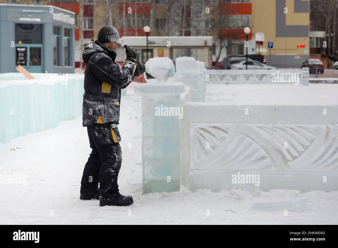 A sculptor carves a round ice ball out of a block of ice with a chisel ...