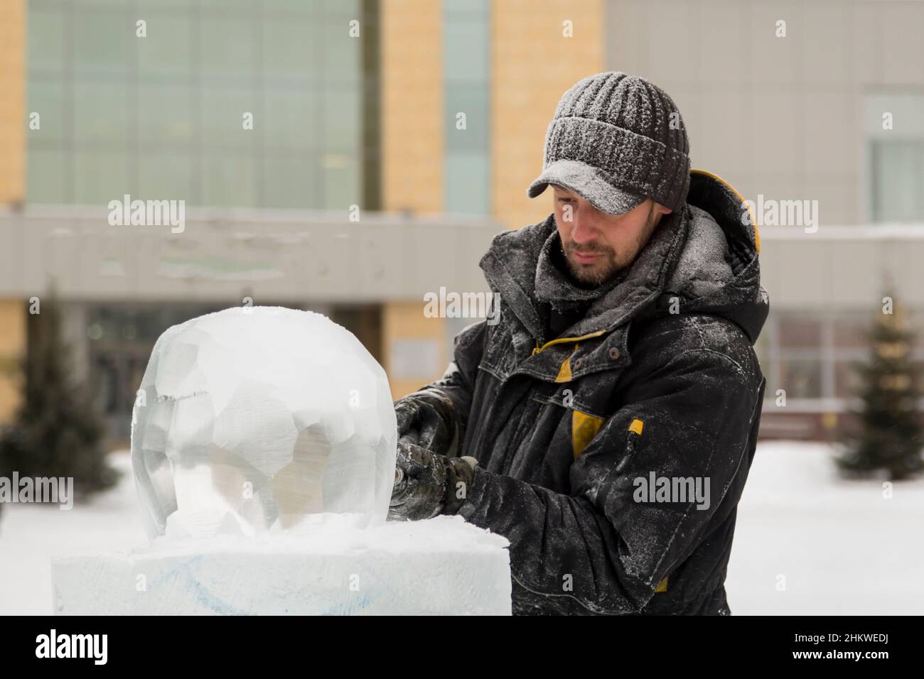 A sculptor carves a round ice ball out of a block of ice with a chisel ...