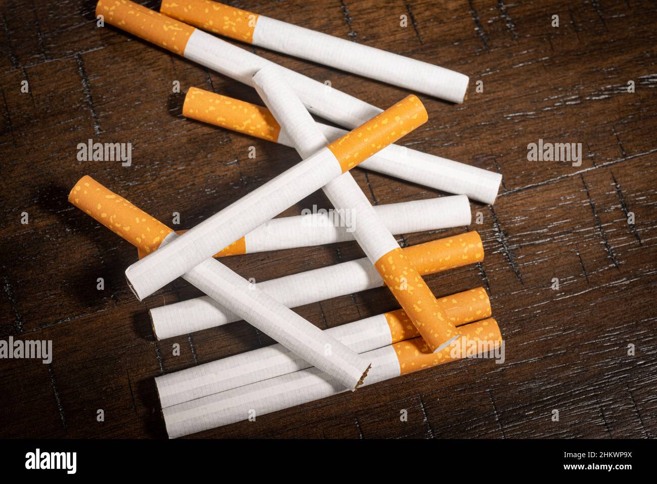 A small pile of loose cigarettes sits on a wooden table. Stock Photo
