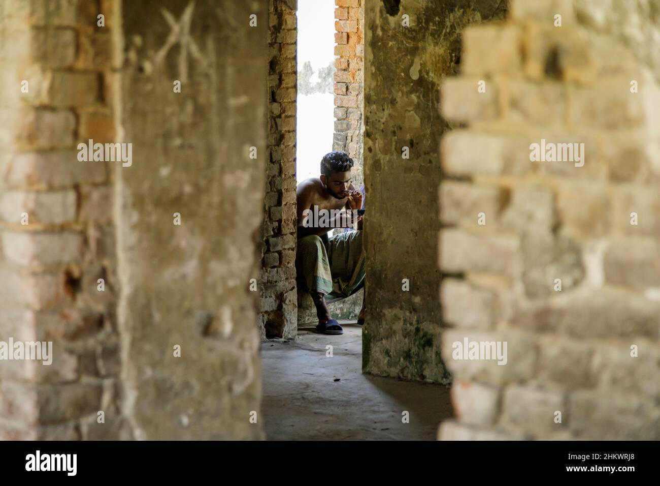 A young man taking a cigarette break in the ruins of the Teota Zamindar Palace in the Manikganj district. The palace, believed to be around 300 years old, had more than 50 rooms originally. Stock Photo