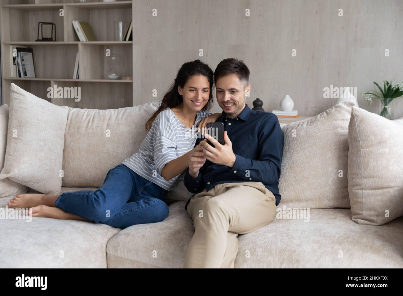 Happy couple using smartphone, relaxing on couch together Stock Photo