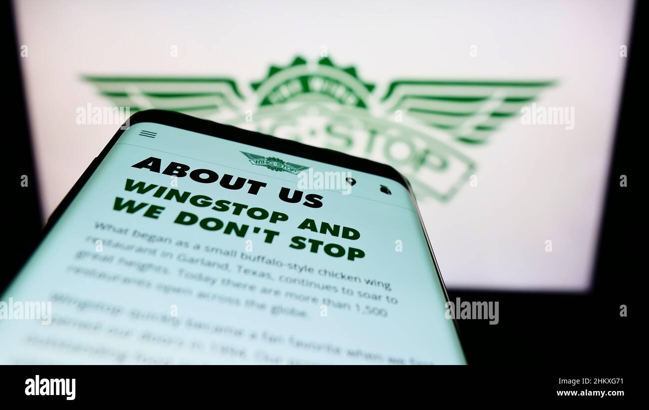 Smartphone with webpage of US gastronomy company Wingstop Restaurants Inc. on screen in front of business logo. Focus on top-left of phone display. Stock Photo