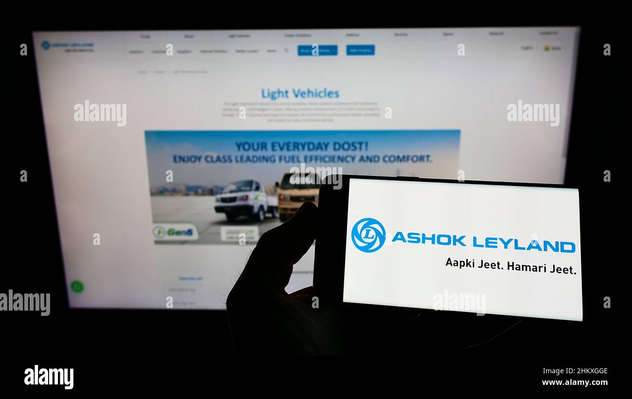 Person holding smartphone with logo of Indian automotive company Ashok Leyland Ltd. on screen in front of website. Focus on phone display. Stock Photo
