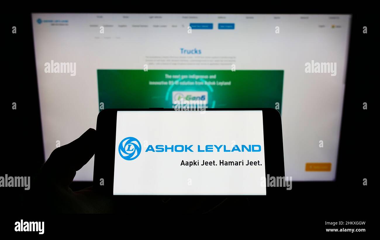 Person holding cellphone with logo of Indian automotive company Ashok Leyland Ltd. on screen in front of business webpage. Focus on phone display. Stock Photo