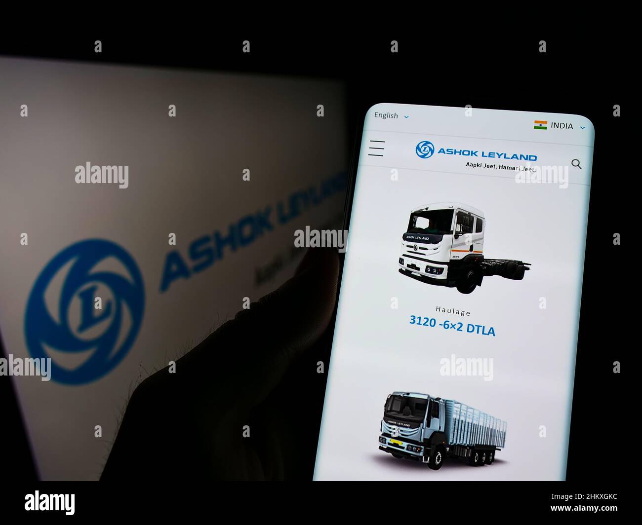 Person holding cellphone with website of Indian automotive company Ashok Leyland Ltd. on screen in front of logo. Focus on center of phone display. Stock Photo
