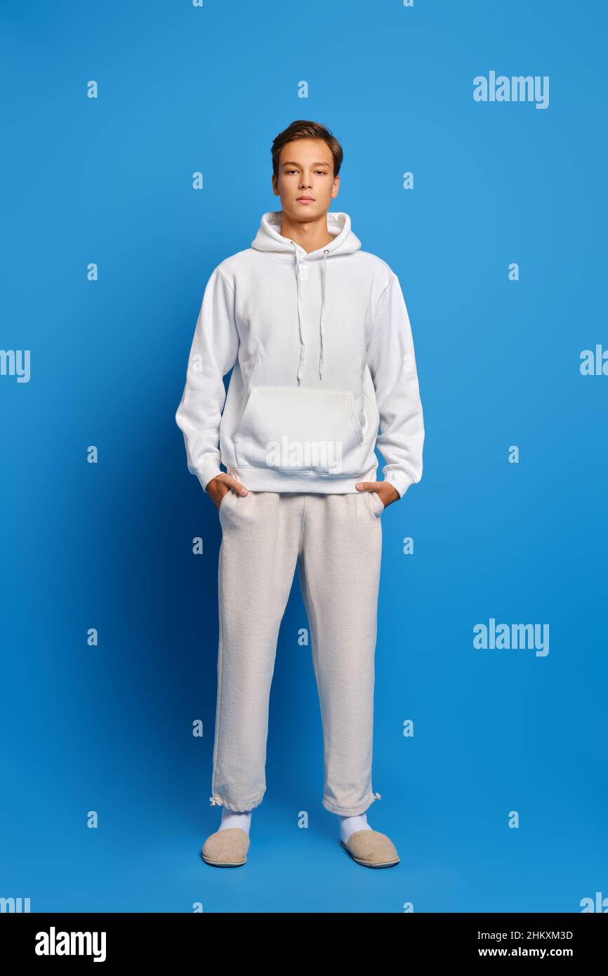 Attractive stylish man wearing white sweatshirt and sweatpants standing over blue studio background Stock Photo