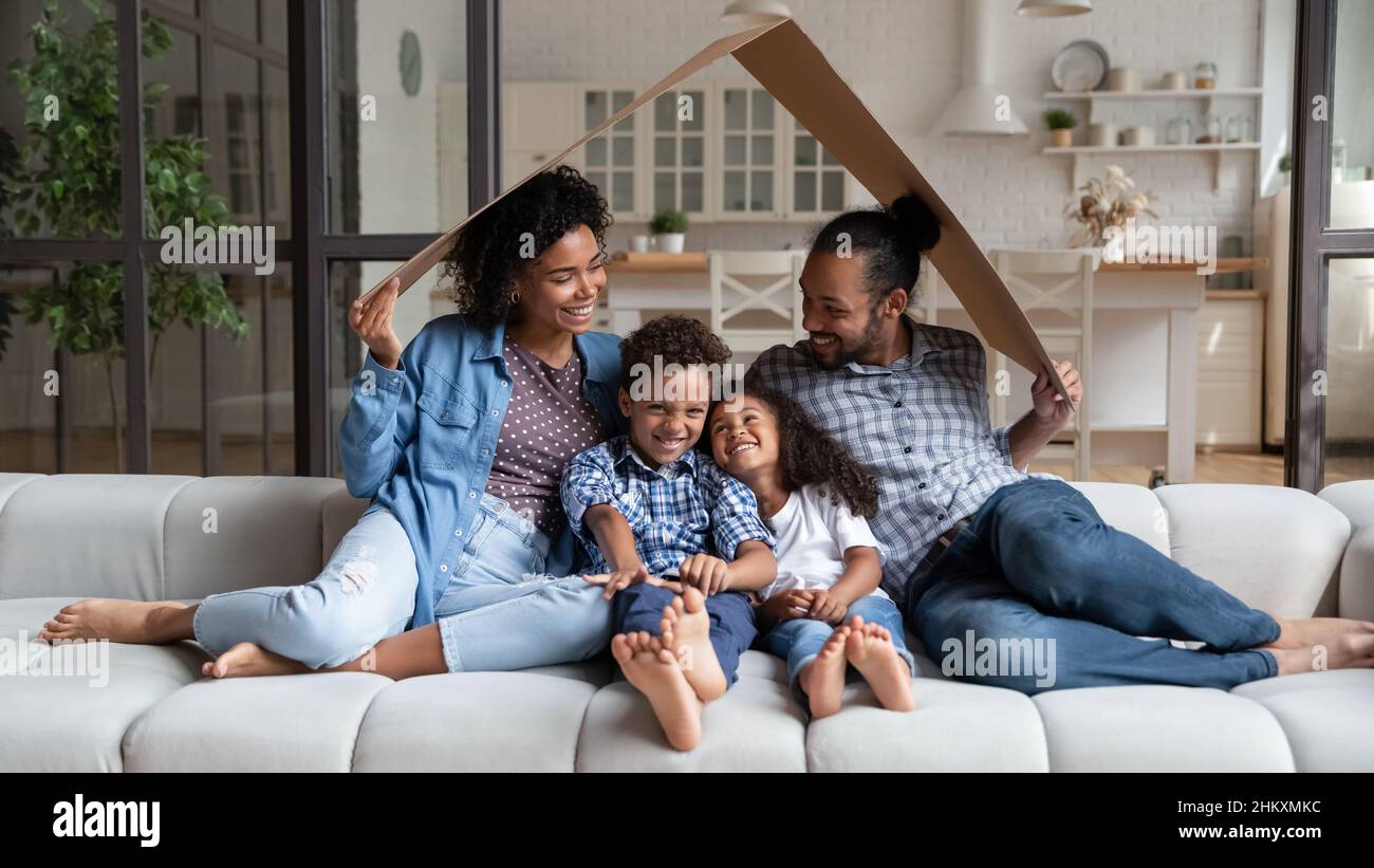Happy loving African American family sitting under carton roof. Stock Photo