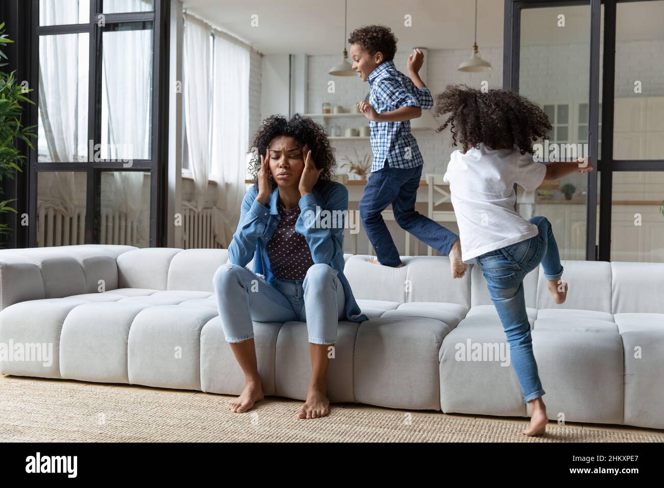 Unhappy young African American mother irritated by loud kids. Stock Photo