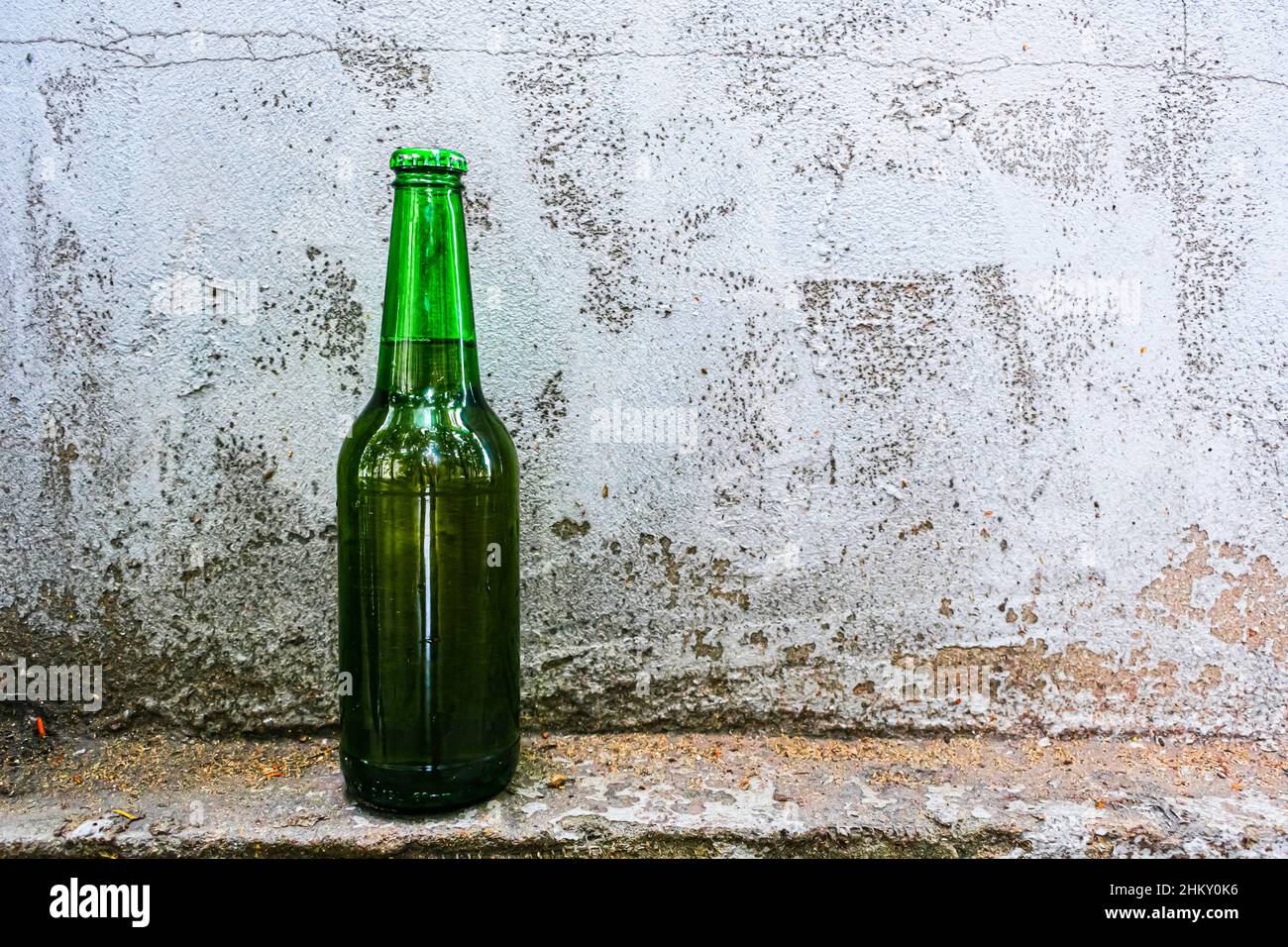 A bottle with an alcoholic drink stands against an old concrete wall Stock Photo