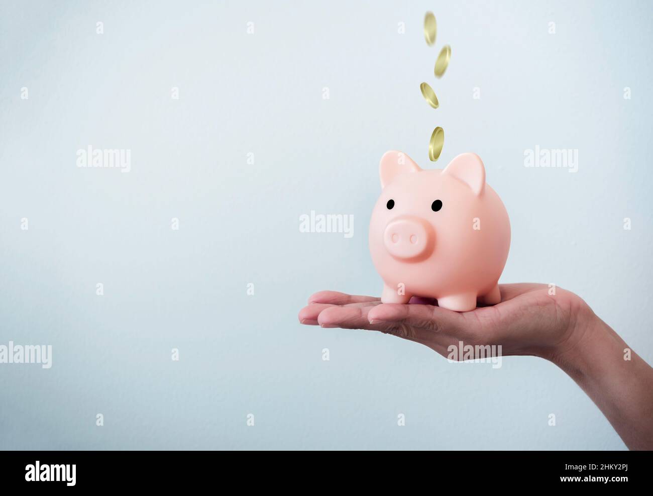 Golden coins fall into the pink piggy bank on a woman's hand on white ...