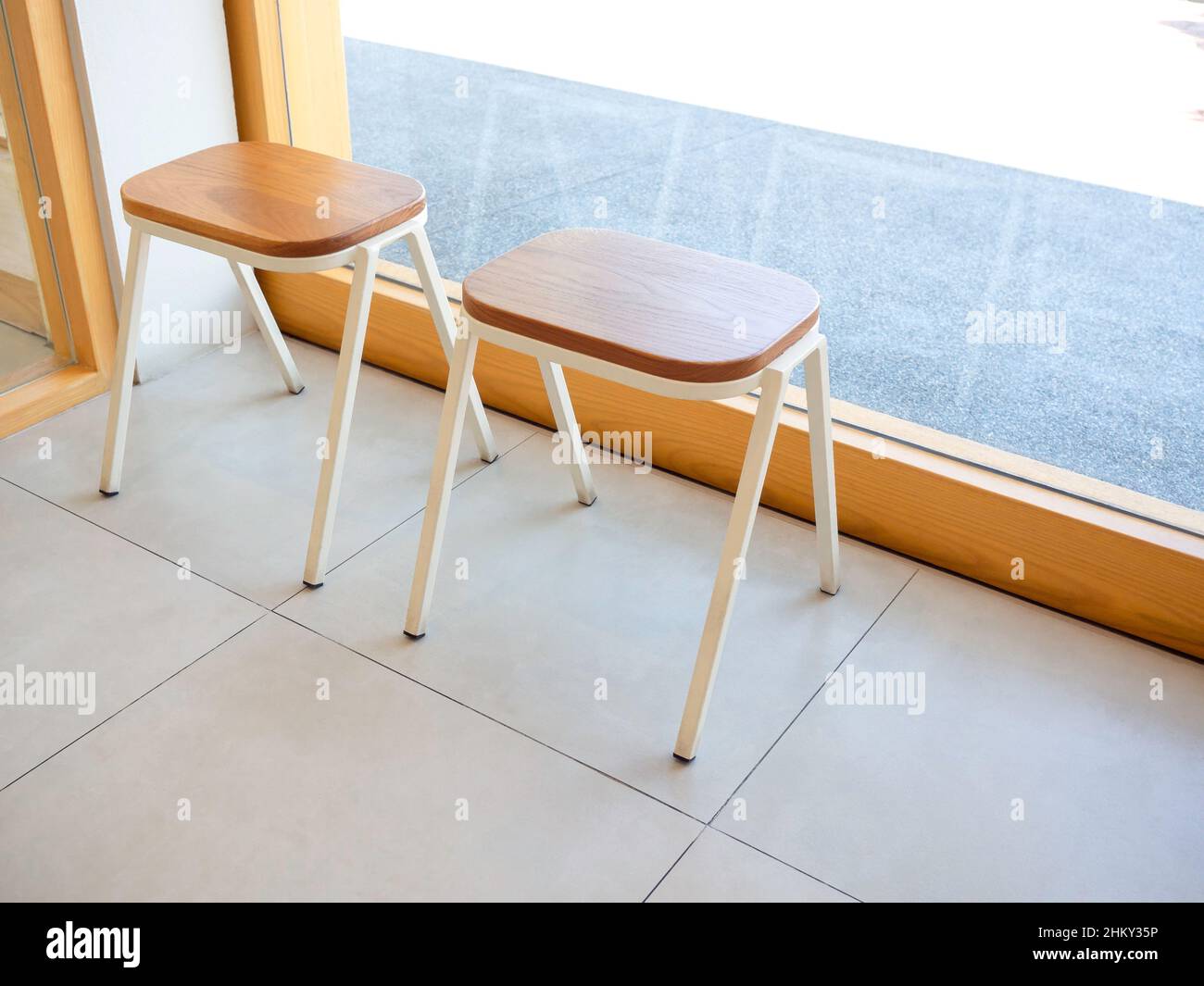 Empty two small wooden chairs without backrest near the glass wall