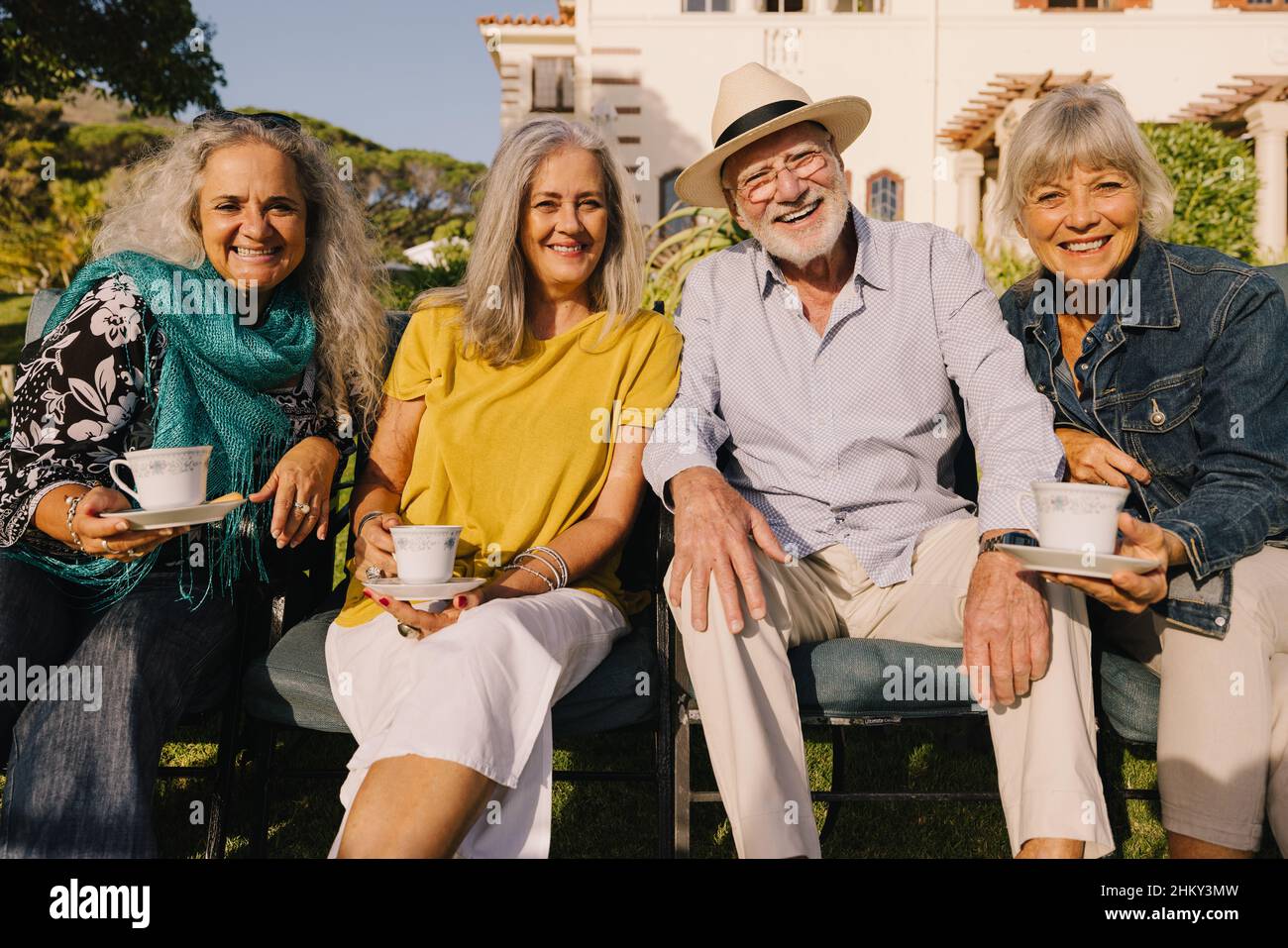 Happy senior citizens smiling at the camera while relaxing outside a retirement home. Group of carefree elderly people having tea together and enjoyin Stock Photo