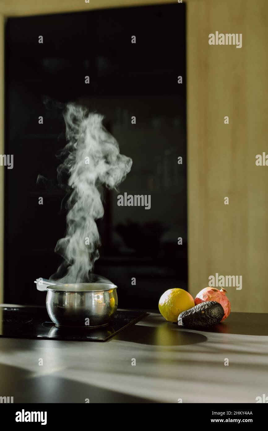 Vertical shot of vegetables near the saucepan on an electric stove with the steam coming out from it Stock Photo