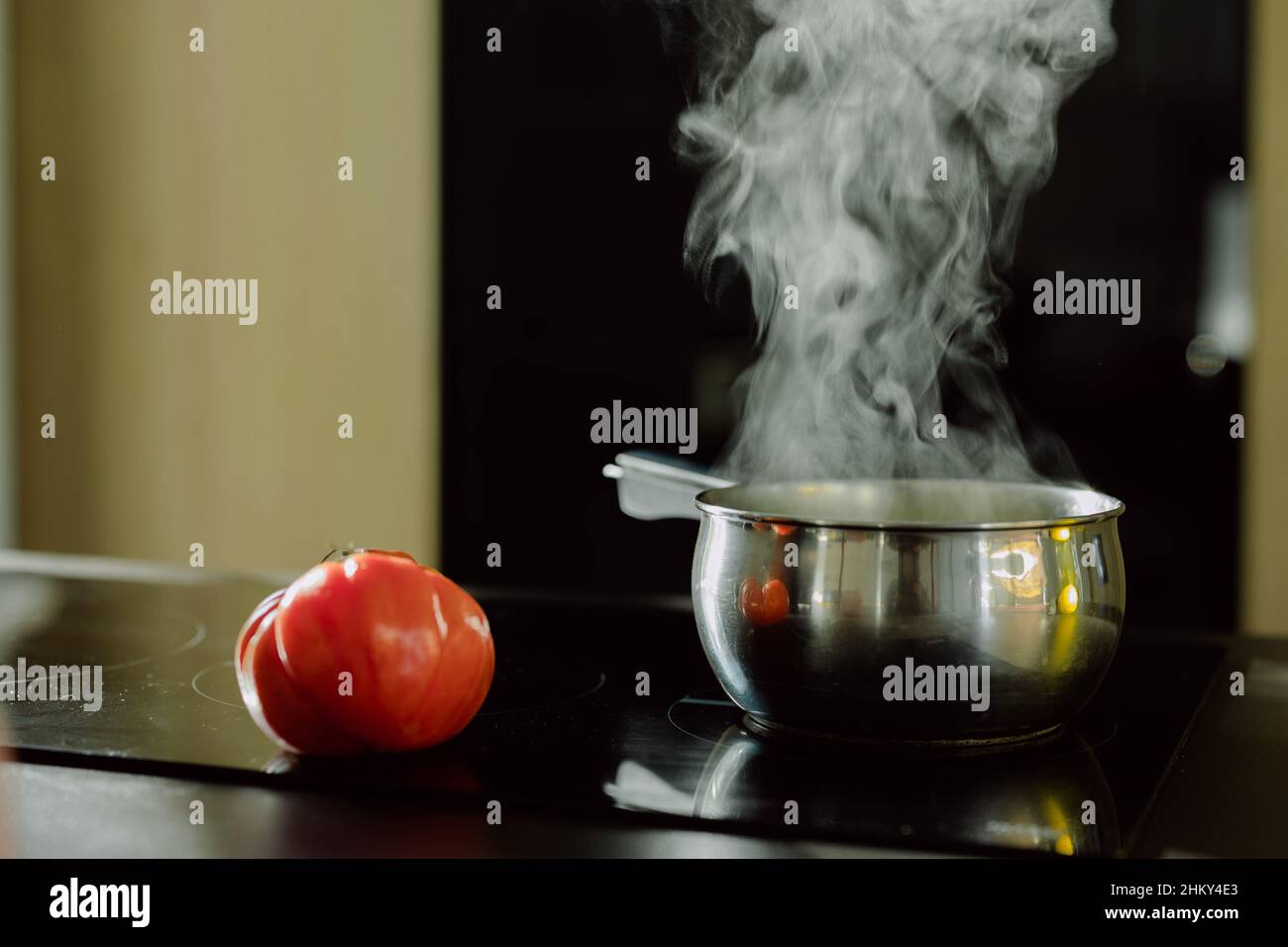 View of the tomato near the saucepan on the electric stove with the steam coming out from it Stock Photo
