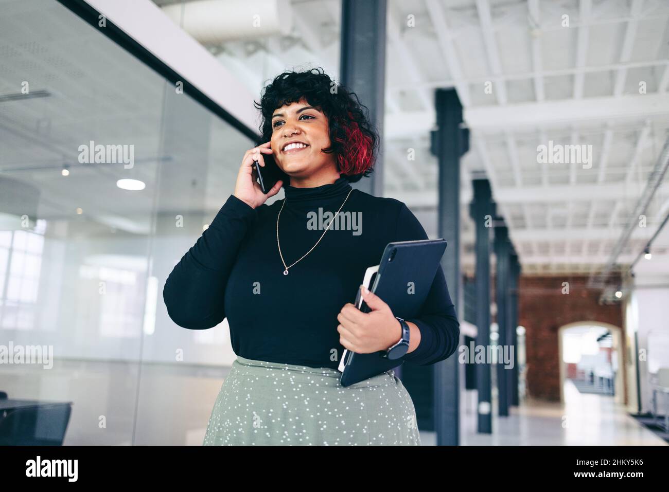 Happy businesswoman taking a phone call in an office. Creative businesswoman closing a business deal over the phone in a modern workplace. Successful Stock Photo