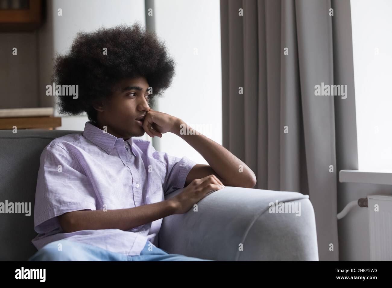 Thoughtful sad teen Black guy sitting on sofa Stock Photo