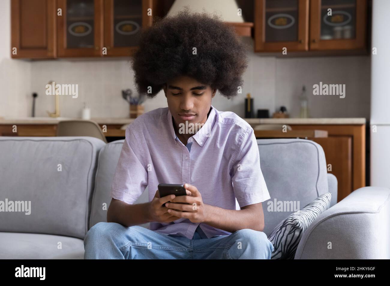 Serious teen African guy with Afro hairstyle typing message Stock Photo