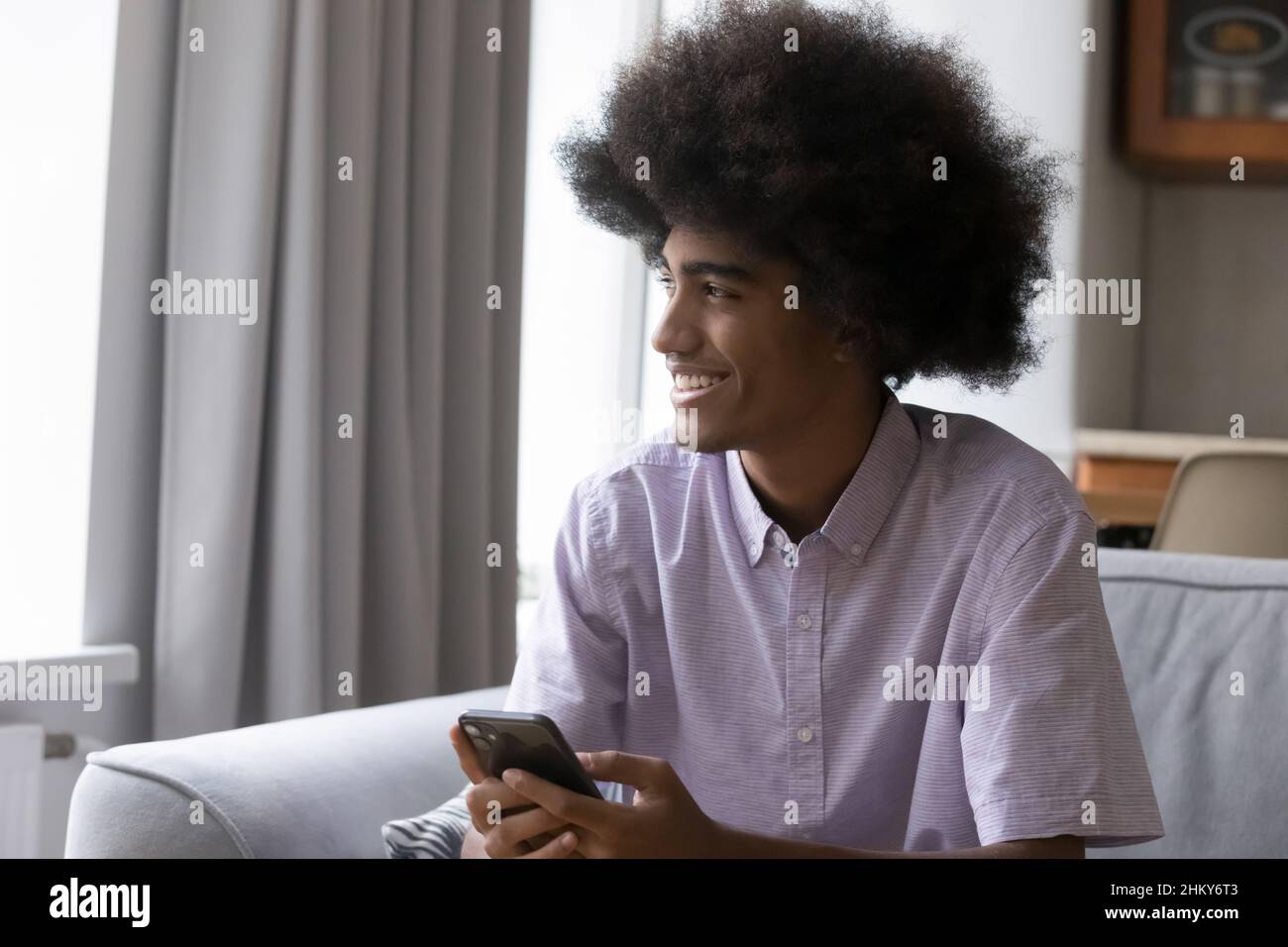 Happy teenage fuzzy haired African guy holding digital gadget Stock Photo