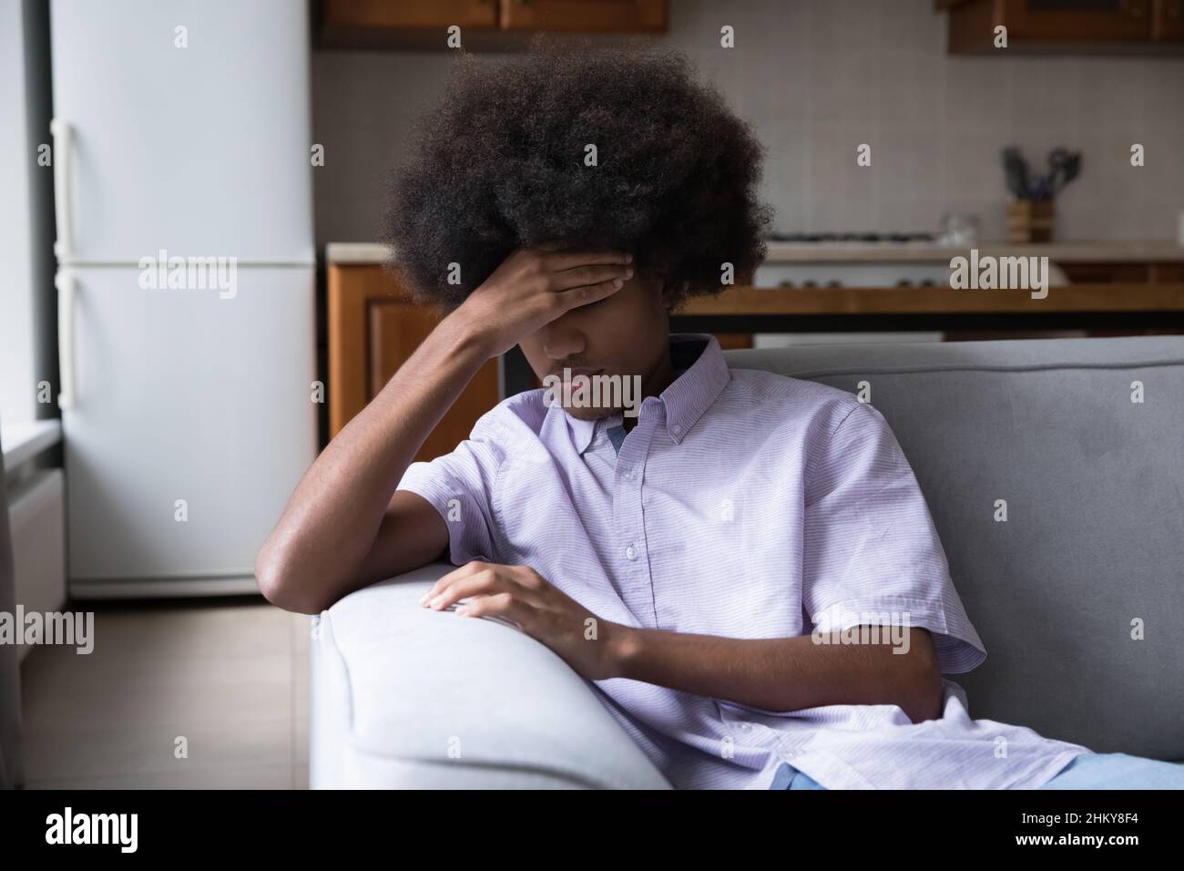 Upset fuzzy haired Black teen guy sitting on couch Stock Photo