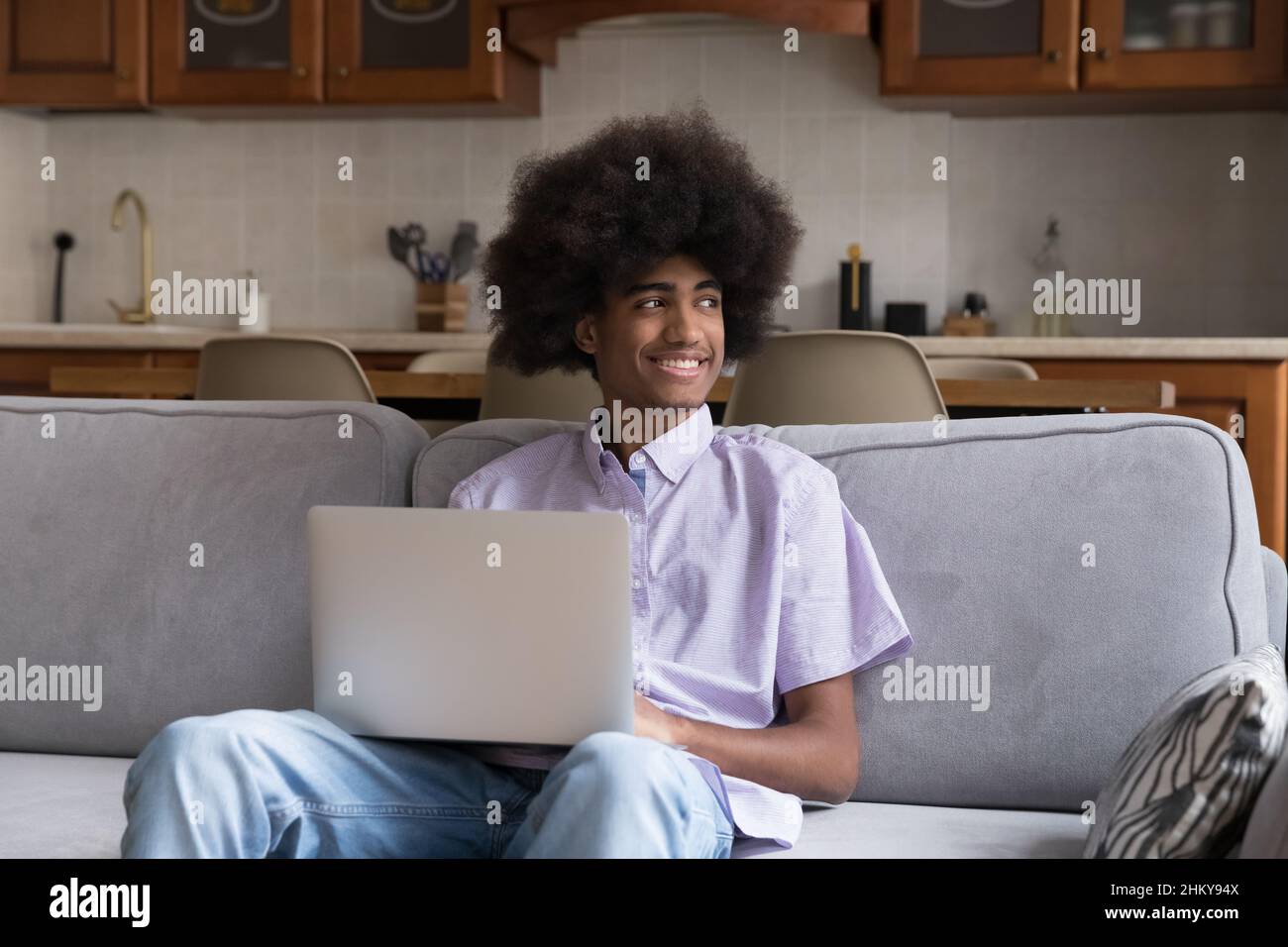 Happy thoughtful Black student guy with Afro hairdo using laptop, Stock Photo