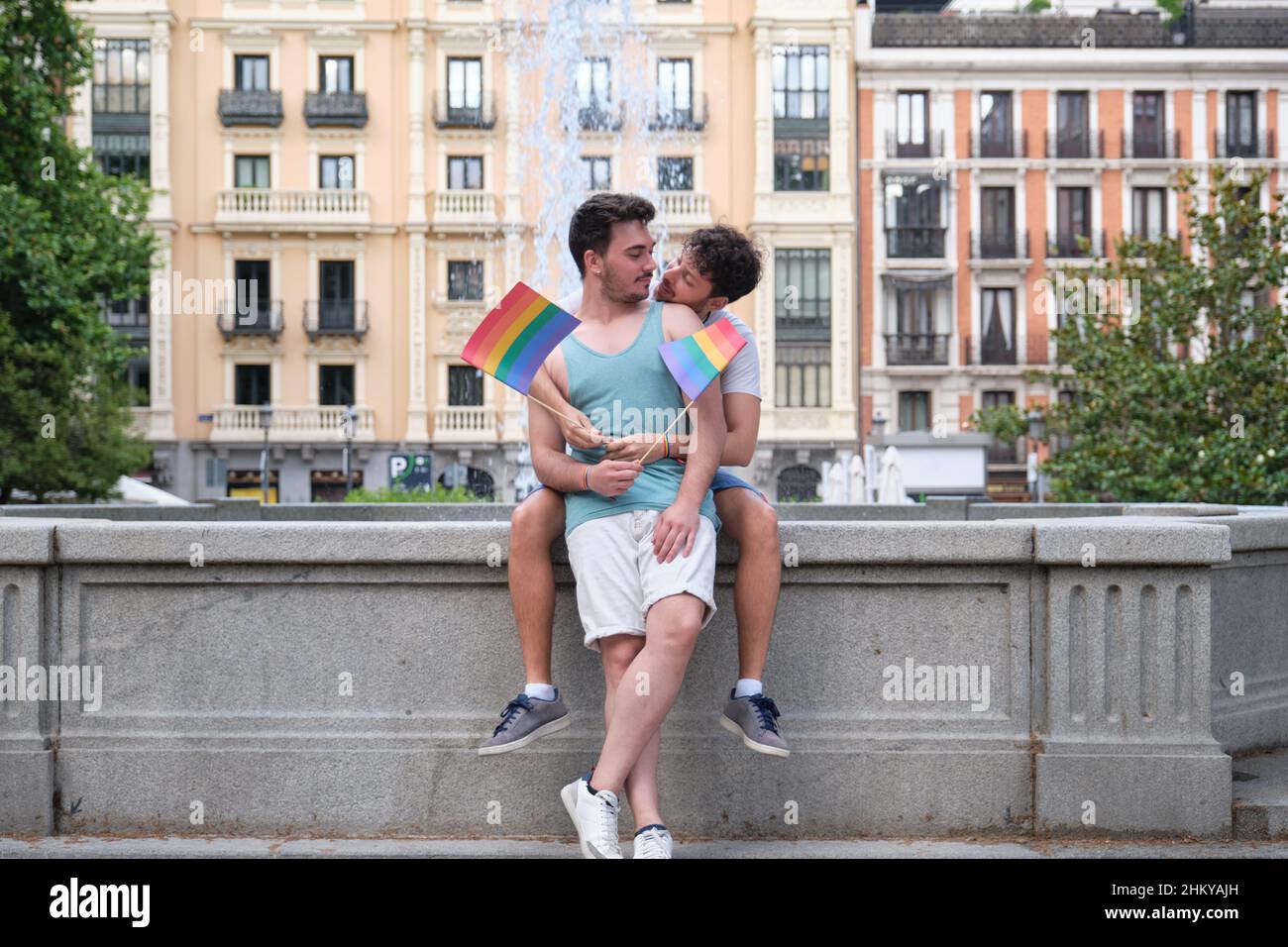 Gay couple about to kiss while hugging sitting near by a font in the street. Stock Photo